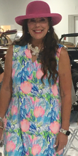 Load image into Gallery viewer, A woman wearing a sleeveless, scalloped neckline, floral print travel dress with a sun visor.